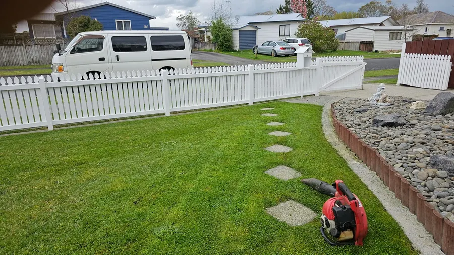 Blower on a fresh front lawn by a white picket fence